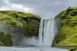 Breathtaking view of Skógafoss waterfall with lush green cliffs in Iceland, showcasing natural beauty.